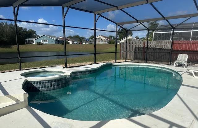 view of swimming pool featuring a patio, glass enclosure, a water view, and an in ground hot tub