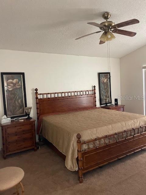 bedroom with ceiling fan, a textured ceiling, and dark carpet