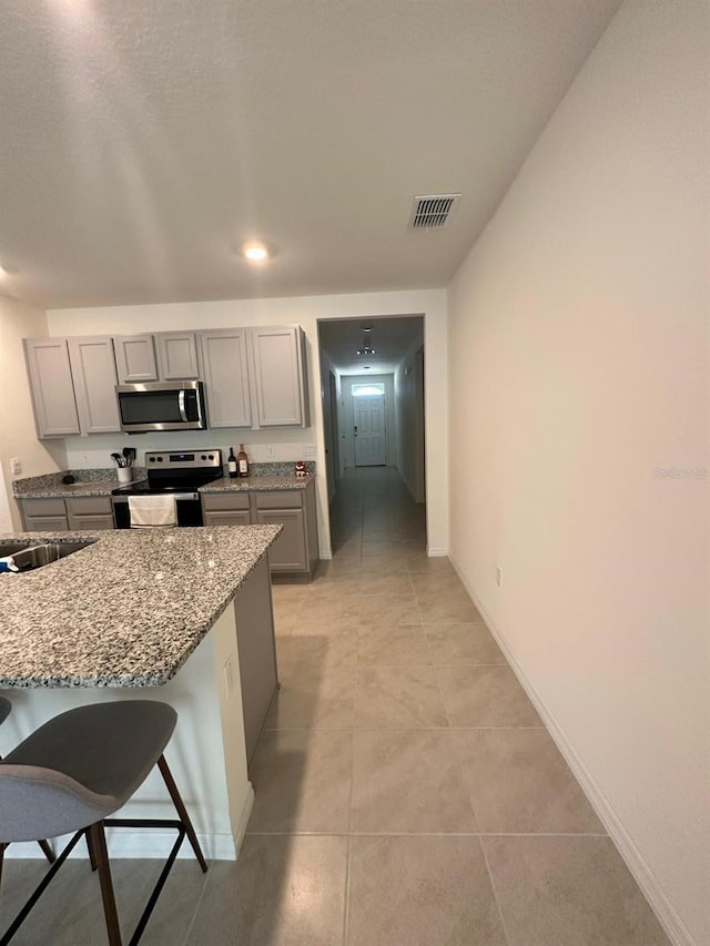 kitchen featuring stainless steel appliances, light stone counters, sink, a kitchen breakfast bar, and gray cabinets