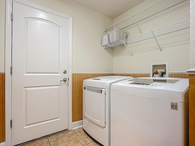 clothes washing area with light tile patterned floors, washing machine and clothes dryer, and wood walls