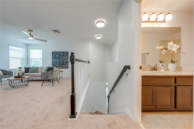 stairway with ceiling fan, sink, and carpet