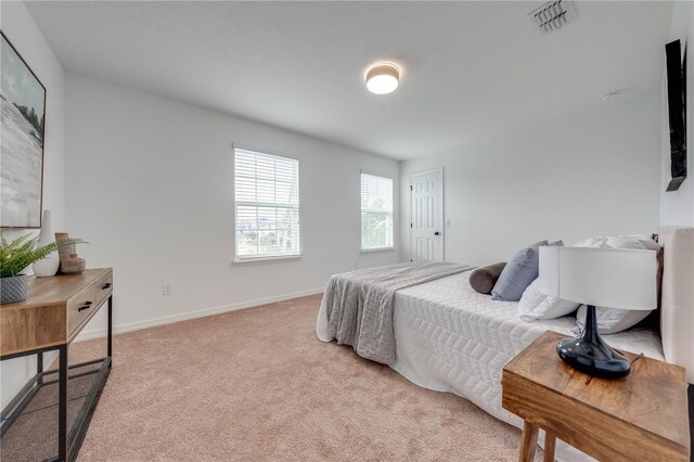 bedroom with baseboards, visible vents, and light carpet