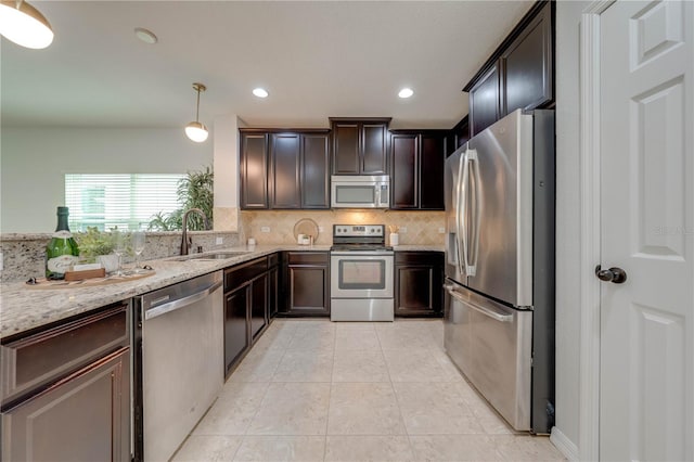 kitchen featuring light stone countertops, sink, hanging light fixtures, stainless steel appliances, and decorative backsplash