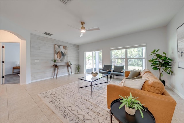 tiled living room featuring ceiling fan and wood walls