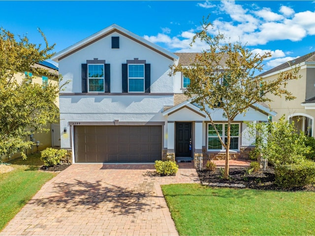 traditional-style home with a front yard, a garage, decorative driveway, stone siding, and stucco siding