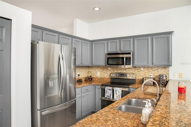 kitchen with decorative backsplash, gray cabinetry, sink, light stone countertops, and appliances with stainless steel finishes