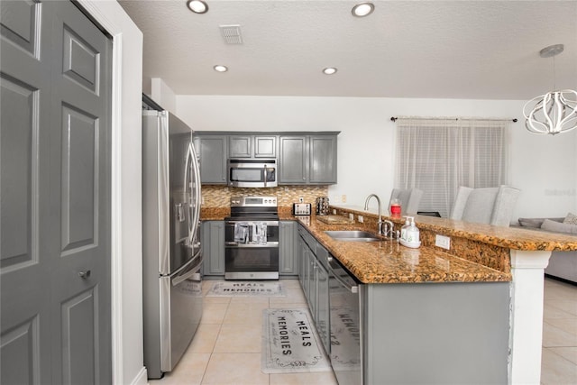 kitchen with gray cabinetry, stainless steel appliances, sink, a kitchen bar, and decorative light fixtures