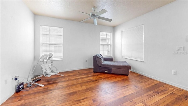 living area with a textured ceiling, a healthy amount of sunlight, dark wood-type flooring, and ceiling fan