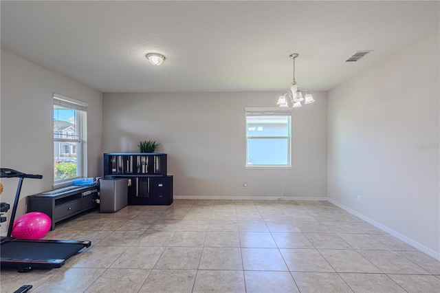 exercise room with light tile patterned floors, a textured ceiling, and an inviting chandelier