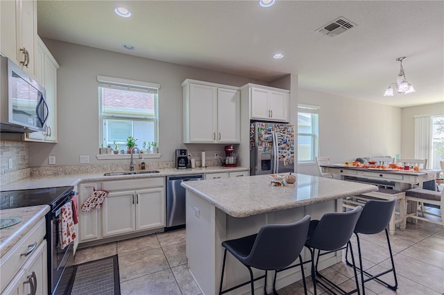 kitchen featuring white cabinets, sink, decorative light fixtures, a kitchen island, and stainless steel appliances