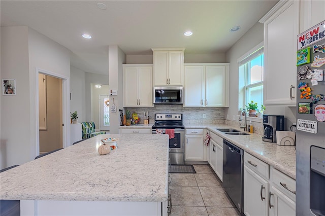 kitchen with decorative backsplash, stainless steel appliances, sink, a center island, and white cabinetry