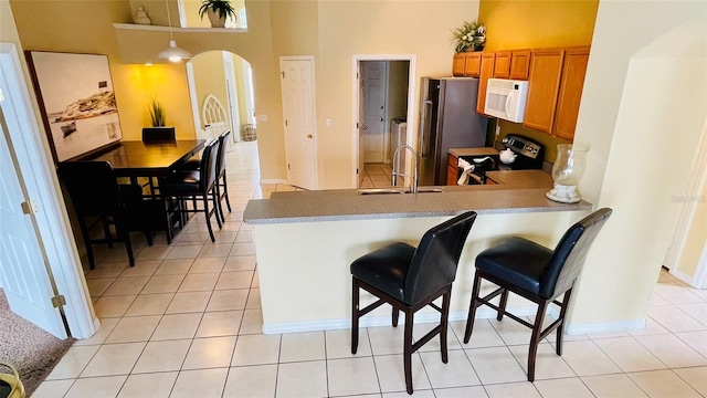 kitchen featuring stainless steel appliances, a towering ceiling, a breakfast bar area, sink, and light tile patterned flooring