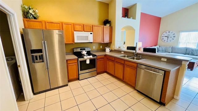 kitchen featuring a towering ceiling, appliances with stainless steel finishes, light tile patterned floors, sink, and kitchen peninsula