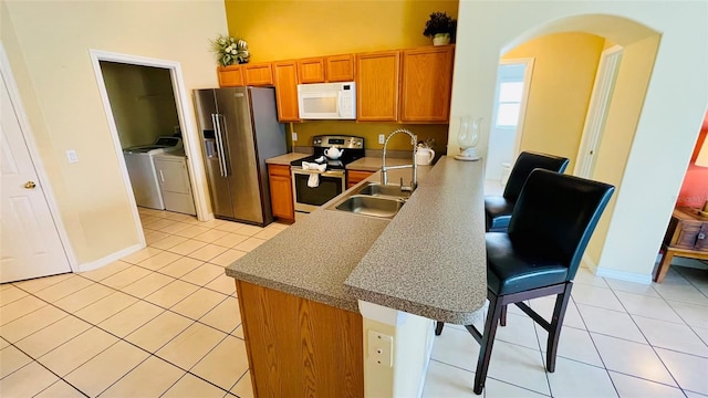 kitchen with appliances with stainless steel finishes, light tile patterned floors, a kitchen bar, sink, and washing machine and clothes dryer