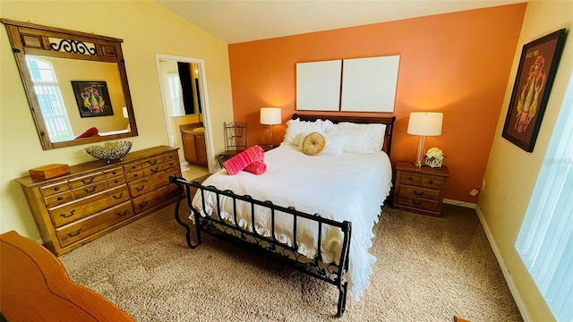 bedroom with ensuite bathroom, light carpet, and lofted ceiling