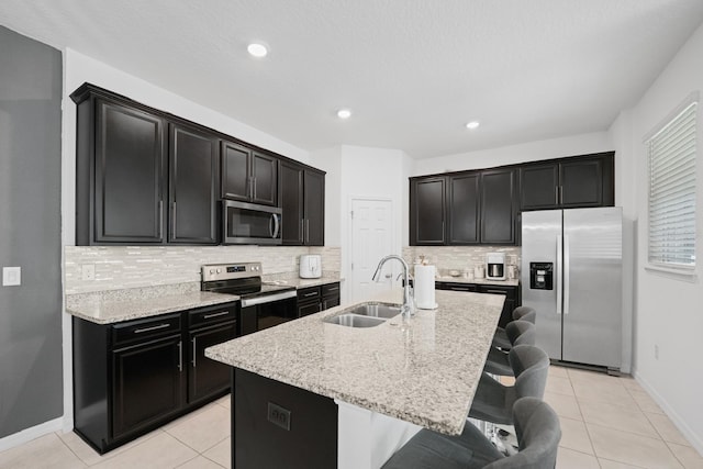 kitchen featuring a kitchen bar, light stone counters, sink, a kitchen island with sink, and appliances with stainless steel finishes