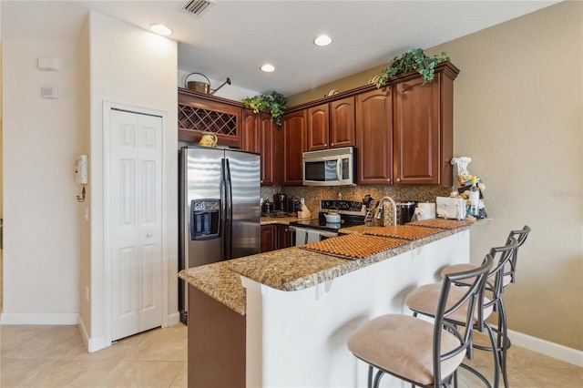 kitchen with stainless steel appliances, a kitchen bar, light stone countertops, decorative backsplash, and kitchen peninsula