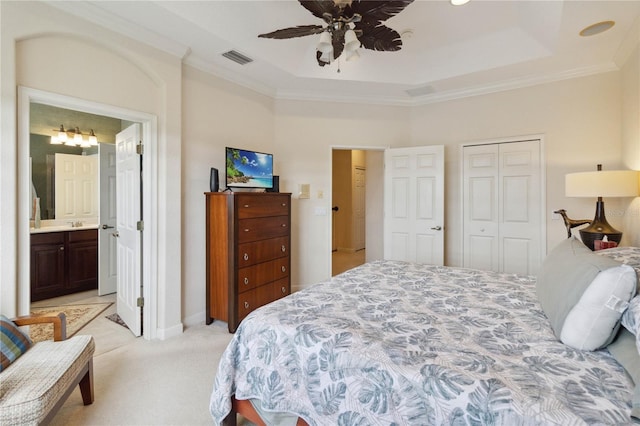 carpeted bedroom featuring ensuite bath, ornamental molding, ceiling fan, a tray ceiling, and a closet