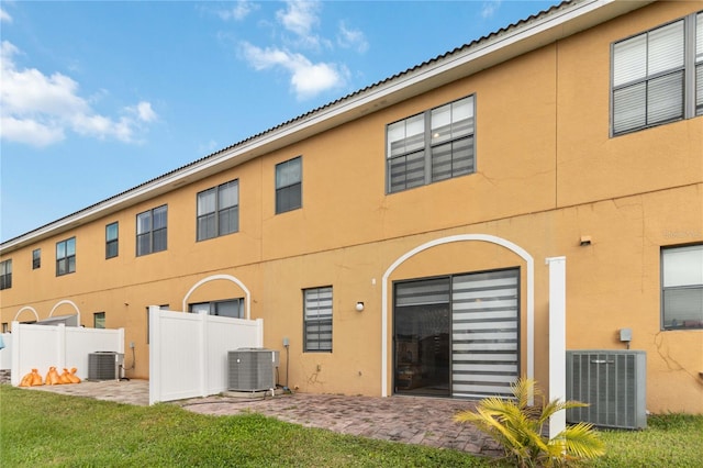 rear view of property with central AC unit, a lawn, and a patio area