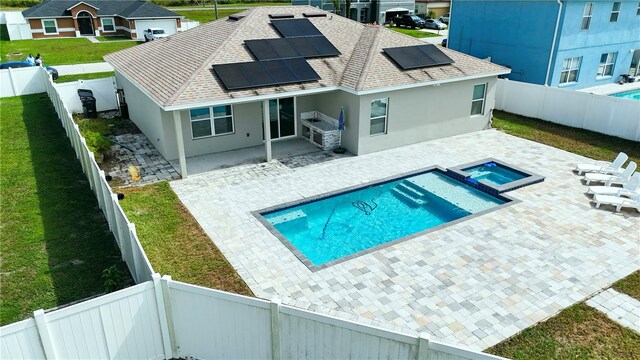 rear view of house with a patio, solar panels, a lawn, and a swimming pool with hot tub