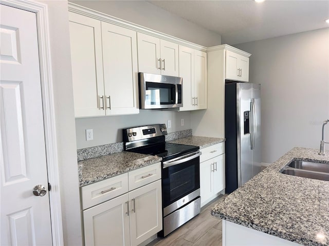 kitchen featuring white cabinets, sink, light stone countertops, light wood-type flooring, and appliances with stainless steel finishes