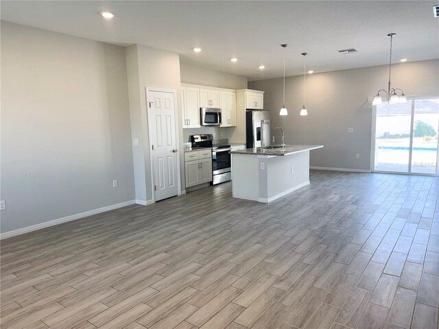 kitchen with a center island with sink, hanging light fixtures, white cabinetry, light wood-type flooring, and appliances with stainless steel finishes