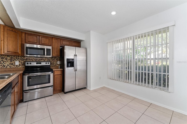 kitchen featuring appliances with stainless steel finishes, a textured ceiling, light tile patterned floors, and tasteful backsplash