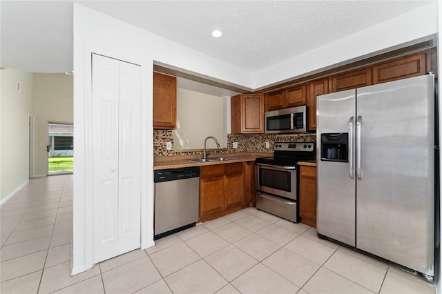 kitchen featuring stainless steel appliances, sink, light tile patterned flooring, a textured ceiling, and tasteful backsplash