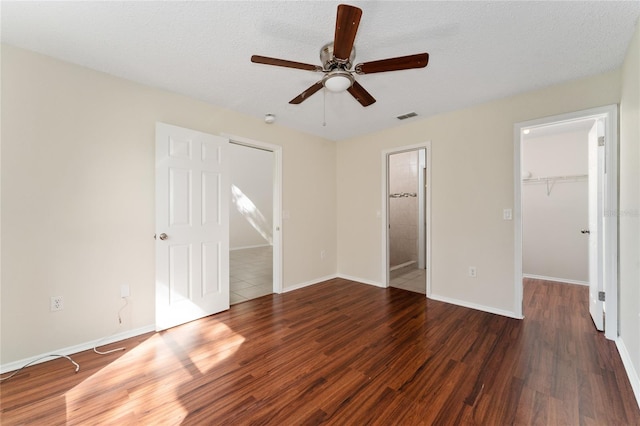 unfurnished bedroom featuring dark hardwood / wood-style flooring, a textured ceiling, a spacious closet, and ceiling fan