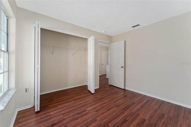 unfurnished bedroom with a textured ceiling, dark hardwood / wood-style floors, and a closet