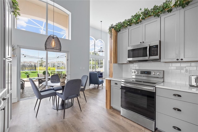 kitchen featuring stainless steel appliances, a high ceiling, decorative light fixtures, gray cabinetry, and light wood-type flooring