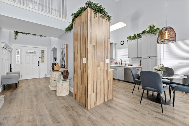 kitchen featuring pendant lighting, sink, dishwasher, a high ceiling, and light hardwood / wood-style flooring