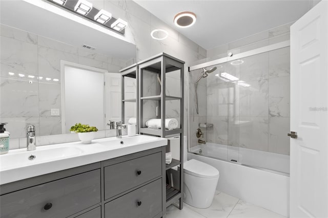 full bathroom featuring toilet, vanity, shower / bath combination with glass door, and tile walls