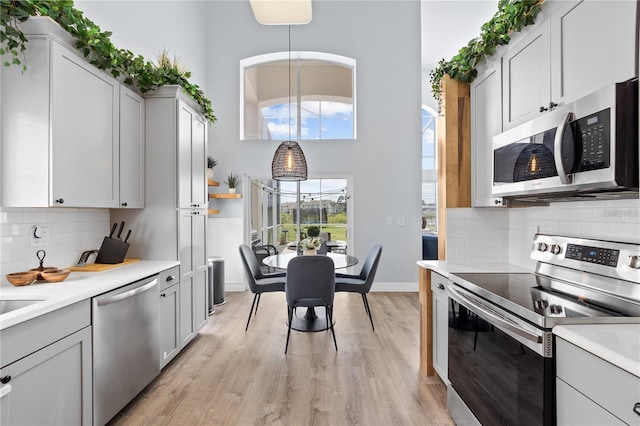 kitchen featuring tasteful backsplash, white cabinetry, appliances with stainless steel finishes, pendant lighting, and light hardwood / wood-style flooring