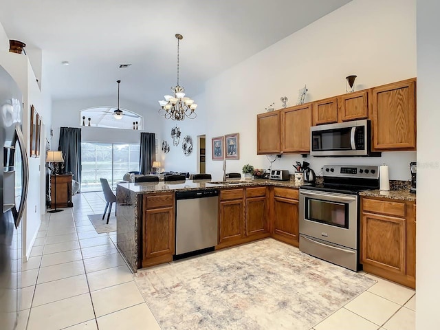 kitchen with kitchen peninsula, appliances with stainless steel finishes, ceiling fan with notable chandelier, decorative light fixtures, and high vaulted ceiling