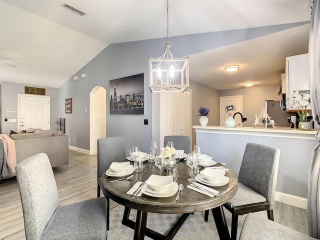 dining space featuring a chandelier, sink, light hardwood / wood-style flooring, and vaulted ceiling