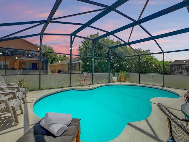 pool at dusk with glass enclosure and a patio area