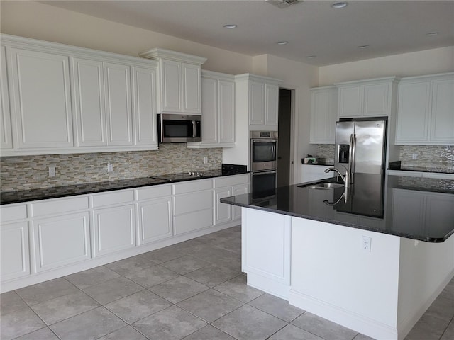 kitchen with white cabinetry, appliances with stainless steel finishes, a center island with sink, and tasteful backsplash