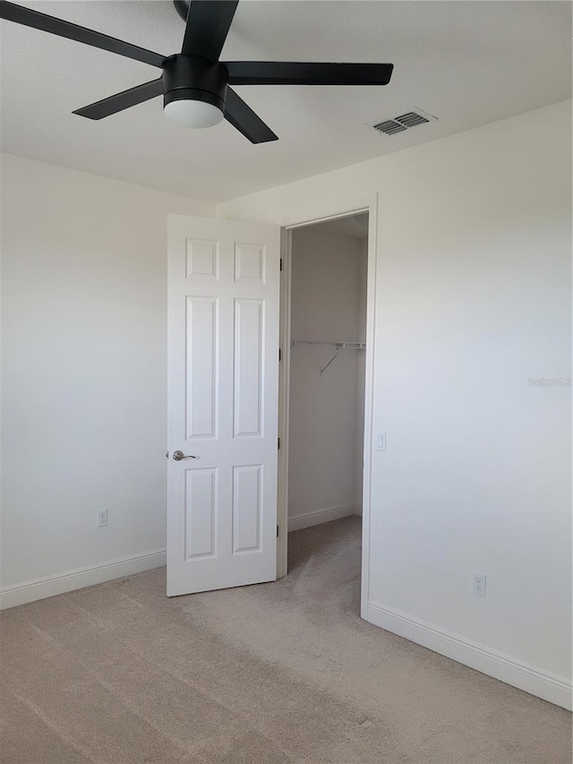 unfurnished bedroom with a closet, a spacious closet, light carpet, and ceiling fan