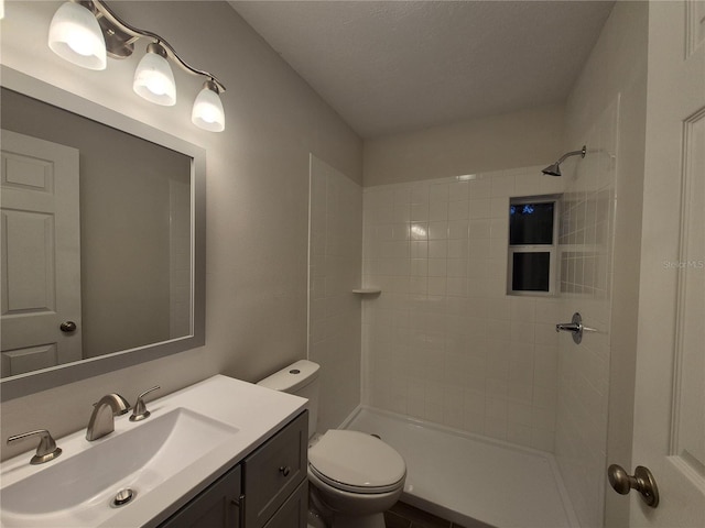 bathroom featuring toilet, vanity, a textured ceiling, and tiled shower