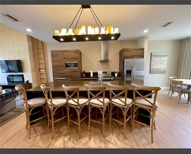 interior space featuring a kitchen breakfast bar, light hardwood / wood-style flooring, hanging light fixtures, appliances with stainless steel finishes, and range hood