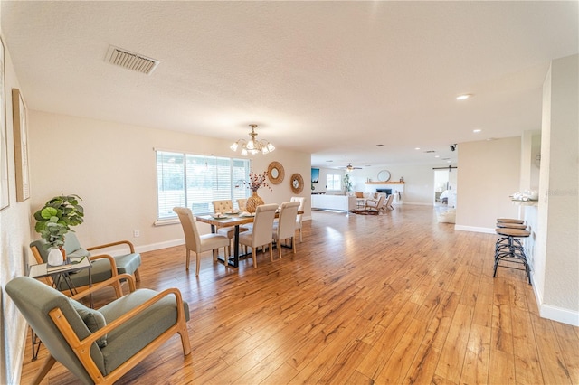 dining space with a chandelier, a textured ceiling, and light wood-type flooring