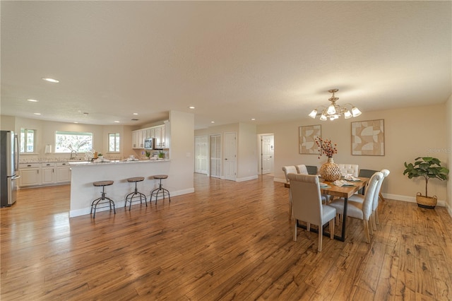 dining area featuring a textured ceiling, a notable chandelier, sink, and light hardwood / wood-style flooring