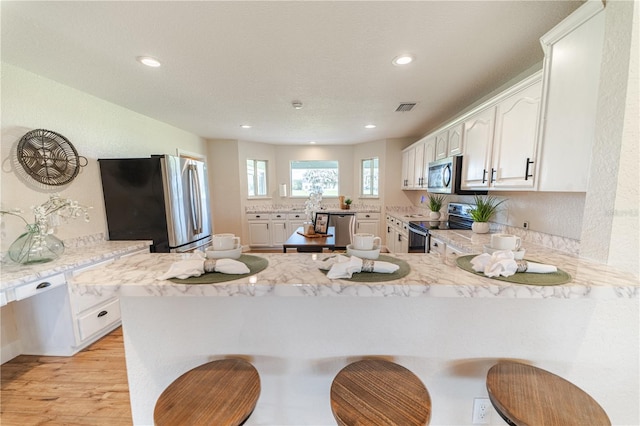 kitchen with white cabinetry, light hardwood / wood-style flooring, kitchen peninsula, a breakfast bar area, and appliances with stainless steel finishes