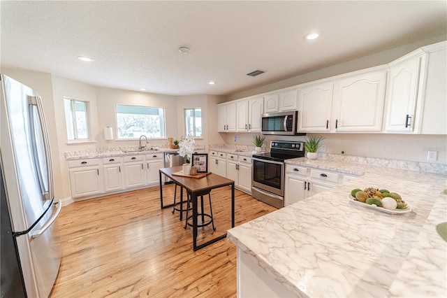 kitchen with white cabinets, sink, light hardwood / wood-style flooring, light stone counters, and stainless steel appliances