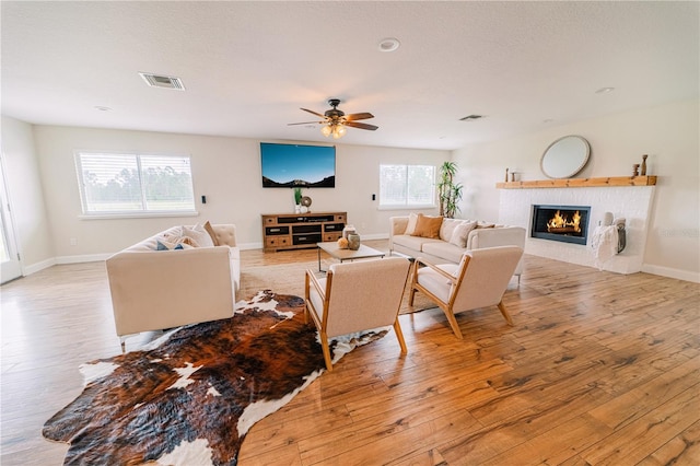 living room featuring a tile fireplace, light wood-type flooring, ceiling fan, and a healthy amount of sunlight