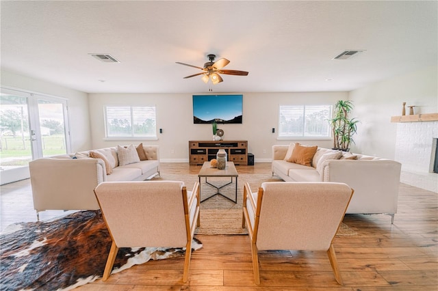 living room with ceiling fan, a fireplace, french doors, and light wood-type flooring