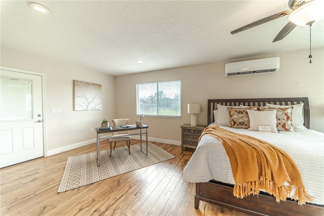 bedroom with a wall unit AC, ceiling fan, wood-type flooring, and a textured ceiling