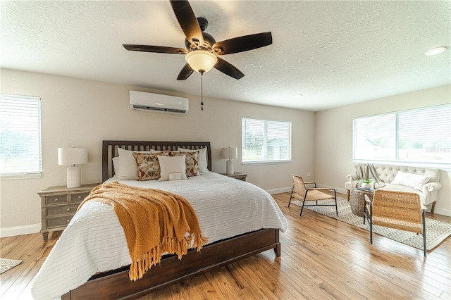 bedroom with ceiling fan, light wood-type flooring, a textured ceiling, and a wall mounted AC