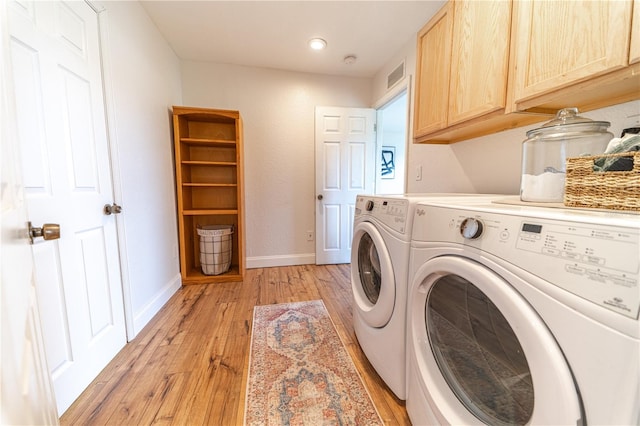 clothes washing area with washer and dryer, light hardwood / wood-style floors, and cabinets